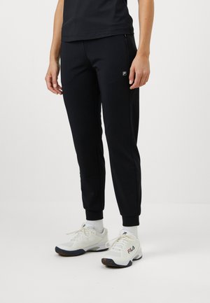 Sorte joggesko med smale ben og mansjetter, med en liten logo på låret. Kombinert med hvite joggesko og hvite sokker.