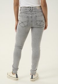 Szürke farmer skinny farmernadrág magas derékkal, íves kialakítású két hátsó zsebbel és fehér varrással. Fehér sportcipővel párosítva.