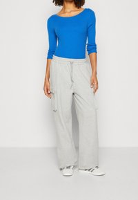 Blue ribbed long-sleeve top with a scoop neckline paired with light grey jogger pants featuring side pockets and an elastic waistband.