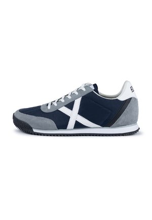 Zapatilla azul marino y gris con materiales de ante y textil, diseño de cruz en blanco, cordones blancos y suela de goma negra con tacos de tracción.