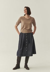 Haut en maille marron à manches courtes associé à une jupe en denim foncé avec des boutons dorés sur le devant. Bottes en cuir marron montant jusqu'aux genoux.