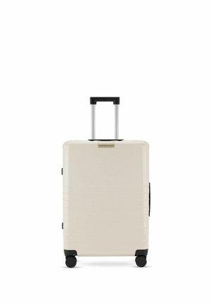 Cremefarbener Hartschalenkoffer mit vier Rollen und schwarzem Teleskopgriff, aufrecht stehend vor weißem Hintergrund.