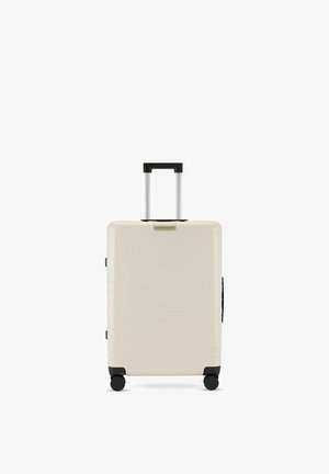 Cream hard-shell suitcase with four wheels and a black telescopic handle, standing upright on a white background.