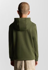 Felpa con cappuccio verde oliva realizzata in un morbido tessuto testurizzato, dotata di tasca a marsupio e polsini a costine, indossata con pantaloni cargo beige.