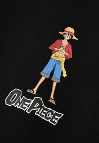 Camiseta negra con un gráfico colorido de un personaje con sombrero de paja, chaqueta roja, pantalones cortos azules y banda amarilla, etiquetado "ONE PIECE."