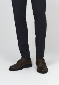 Prune nahkased topelt munkade rihmad, millel on poleeritud viimistlus, koos tumeda tumesinise pükstega, mis esitlevad elegantset disaini ja minimaalset riistvara.