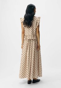 Robe maxi en tissu beige à pois noirs, avec des manches volantes et un design à niveaux. Assortie avec des chaussures plates noires.