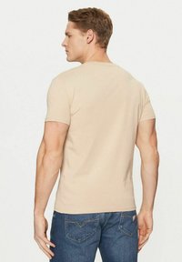T-shirt beige a maniche corte vista da dietro, con scollo arrotondato e tessuto liscio. Abbinata a jeans di denim blu con due tasche posteriori.
