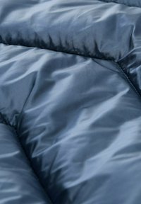 Námornícky modré prešívané tkanivo s hladkou, lesklou textúrou, s horizontálnymi švami vytvárajúcimi „nafúknutý“ vzhľad. Žiadne vzory ani kovové komponenty nie sú viditeľné.