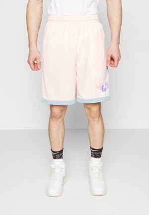 Mann trägt hellrosa Basketballshorts mit blauer Einfassung, schwarze gemusterte Socken und weiße High-Top-Sneaker, steht vor einem schlichten Hintergrund.
