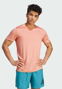 Camiseta deportiva de color rosa claro con mangas cortas y cuello redondo, hecha de tejido que absorbe la humedad, combinada con pantalones cortos azules con un logo negro.
