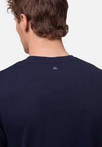 Tmavě modré bavlněné tričko s kulatým výstřihem, krátkými rukávy a malým logem na zádech ve světle modré barvě.