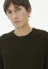 Tumši zaļš teksturēts džemperis ar ribinātu apkakli, kas piedāvā brīvu piegriezumu un smalku rakstu, veidots ar ikdienišķu stilu.