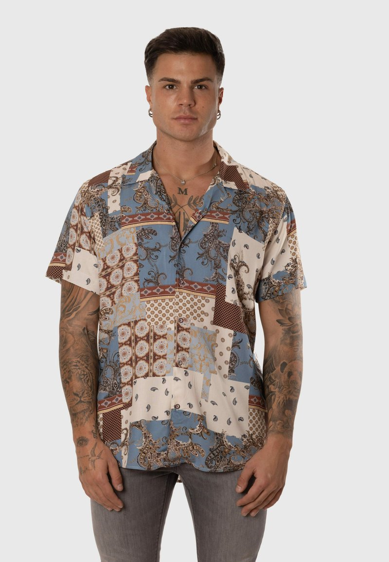 Camisa de manga corta con un diseño de patchwork en tonos azul, marrón y crema, con intrincados patrones florales y un cuello tipo solapa.
