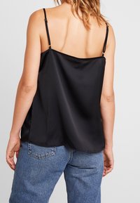 Svart satängcamisole med justerbara tunna remmar, slät textur, lös passform och rundad fåll, i kombination med ljusblå denimjeans.