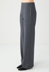 Navy wijde broek met een geometrisch patroon, voorzien van een gladde textuur en een getailleerde pasvorm. Compleet met puntige zwarte schoenen.