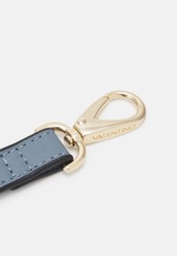 Fermeture en métal doré attachée à une sangle en cuir bleu avec un accent noir, présentant une texture lisse et des détails de couture.