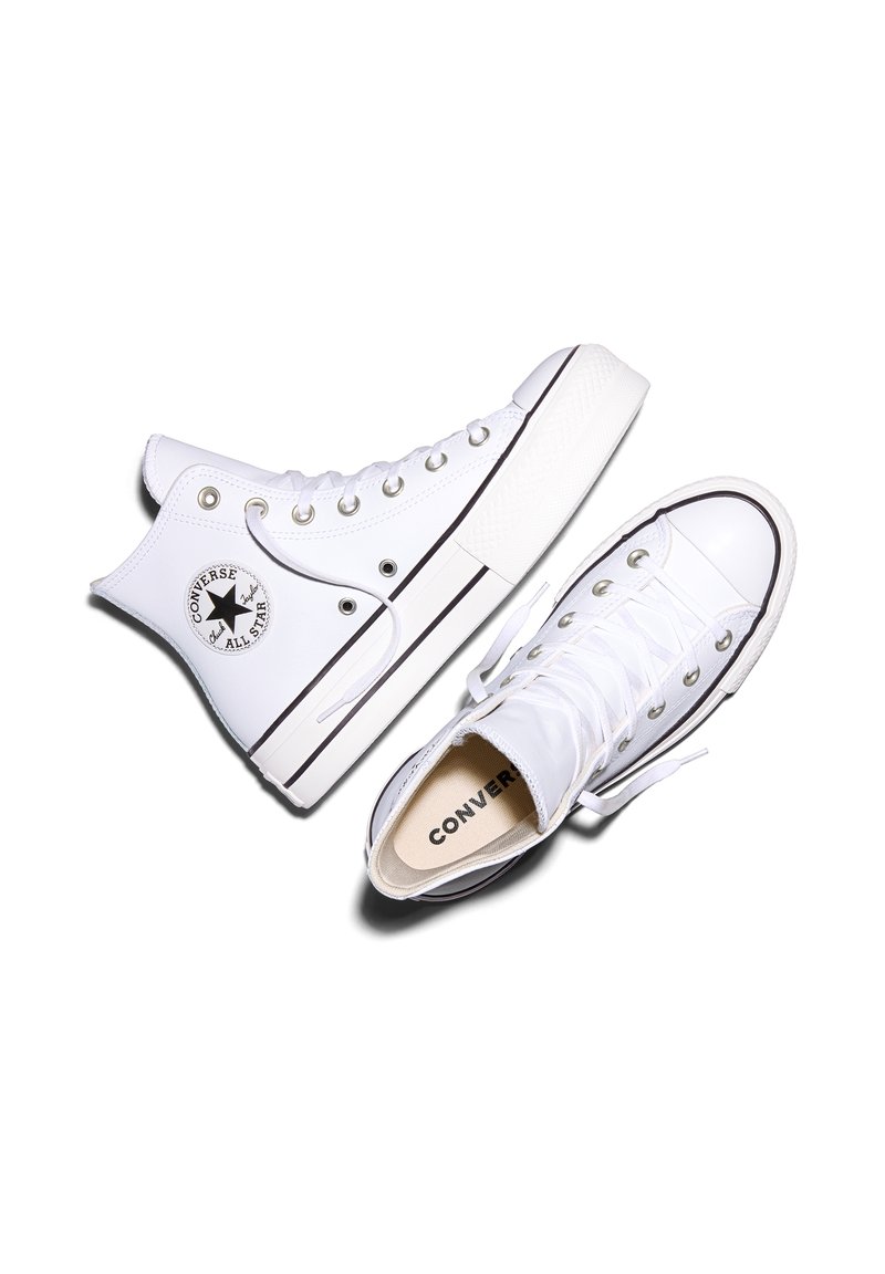 Baskets montantes blanches Converse avec logo étoile noir sur le côté, lacets blancs et semelles en caoutchouc à rayures noires sur fond blanc.
