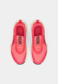 Ναϊκη παπούτσια σε φωτεινό ροζ διχτυωτό υλικό με υφή, διαθέτοντας μαύρες λεπτομέρειες και στρογγυλή κρεμ σόλα. Κορδόνια και λογότυπο στη γλώσσα.