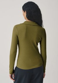 Olivengrøn langærmet top med ribbet struktur og afslappet pasform, med krave og buet kant, kombineret med mørke bukser.