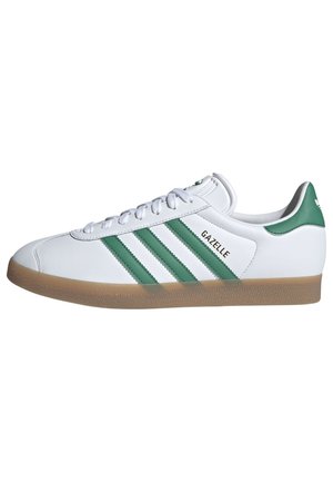 Basket Adidas Gazelle blanche avec des bandes vertes et un languette au talon, semelle en gomme naturelle et lacets blancs, vue de côté.