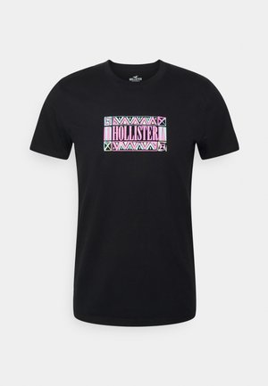 Zwart T-shirt met korte mouwen, voorzien van een kleurrijk geometrisch patroon en de tekst "HOLLISTER" in het midden van de borst.