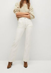 Jeans in denim bianco con taglio dritto, cuciture chiare e due tasche frontali. Abbinati a un maglione in knit beige e stivali con tacco marroni.