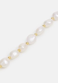 Tjock pärlhalsband som har oregelbundet formade vita pärlor, blandat med små guldpärlor, mot en ljus bakgrund.
