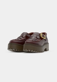 Bordeaux leren plateau schoenen met een geweven voorkant, een verstelbare gouden gesp en dikke gestructureerde rubberen zolen voor grip.