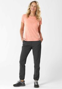 Camiseta de manga corta en color coral con un patrón sutil, combinada con pantalones negros ajustados y zapatillas deportivas grises. Corte relajado, textura suave.