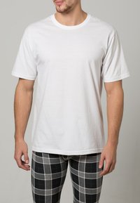 Camiseta blanca de manga corta hecha de algodón. Presenta un diseño clásico de cuello redondo. Combinada con pantalones de cuadros grises.