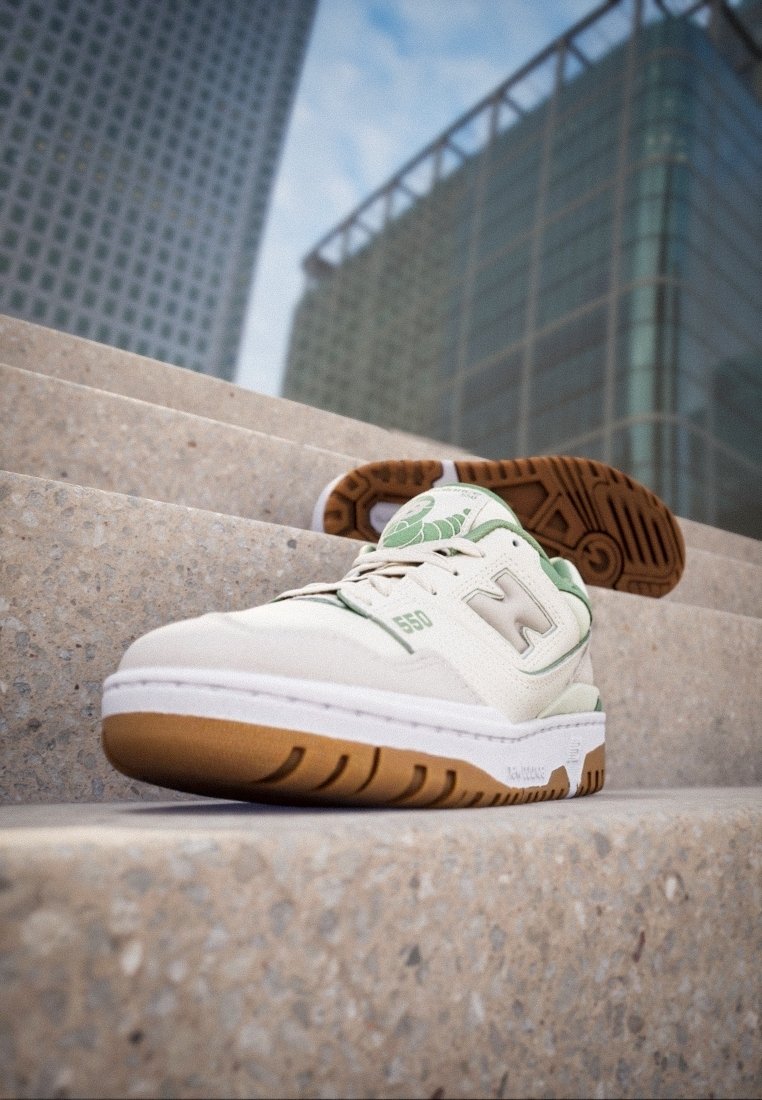 Baskets en cuir blanc avec des accents verts et une semelle extérieure en caoutchouc marron, présentant un motif texturé et un logo bien visible sur le côté.