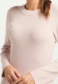 Ljusrosa ribbad tröja med rund hals och långa ärmar, med en strukturerad tygkvalitet och lätt utställda ärmslut.