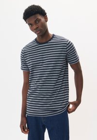 Jūrinės ir šviesiai pilkos juostelėmis marškinėliai, pagaminti iš minkštos medvilnės, su apvalia iškirpte ir trumpomis rankovėmis, derinami su mėlynais džinsais.