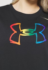 Svart t-shirt med en stor, färgglad regnbågs Under Armour-logotyp. Logotypen har en penseldesign med röd, orange, gul, grön och blå.