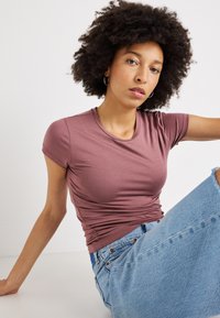 Lühikeste varrukatega, ümber keha istuv t-särk mauve'ist kangast, millel on sile tekstuur. Stiilitud kergelt rullitud varrukatega, koos heledad sinised kulunud teksapüksidega.