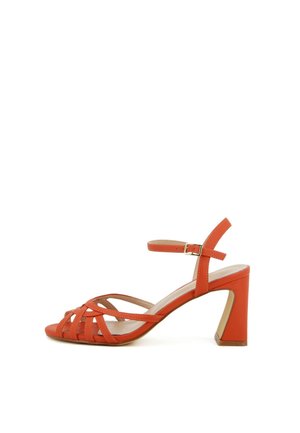 Sandalo arancione con tacco alto a blocco, punta aperta, cinturini incrociati e cinturino alla caviglia con fibbia dorata, su sfondo bianco.