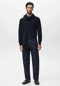 Jersey de lana azul marino con una bufanda larga a juego, pantalones de mezclilla oscuros y zapatos de cuero negros. La bufanda presenta un sutil detalle de flecos.