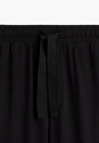 Czarne dresy z bawełny mają elastyczny pas z sznurkiem. Materiał jest gładki i lekko rozciągliwy, bez widocznych wzorów.