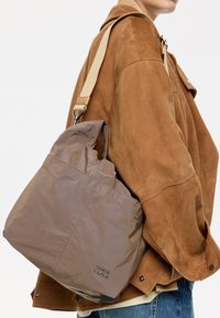 Bolso de hombro de nailon marrón con una textura suave, que presenta una apertura fruncida, correa ajustable y detalle de logo en relieve.