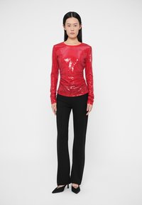 Punastest litritest pikkade varrukatega pluus, mis on kombineeritud mustade pükstega. Pluusil on keha järgnev lõige ja sile tekstuur, pükstel sirge lõige.