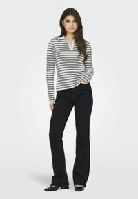 Stribet langærmet top i sort og hvid med V-hals design, parret med flagrende sorte jeans og sorte sko.