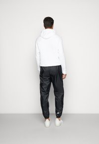 Vit hoodie med en stor huva, kombinerad med svarta, lätta, tapered joggarbyxor. Har elastiska mudd och vita sneakers som accent.