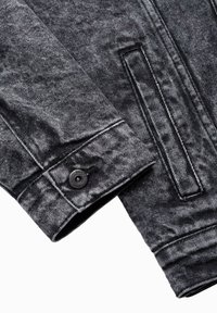 Giacca di jeans grigia con finitura testurizzata, caratterizzata da un dettaglio con bottoni e cuciture in contrasto. Collo e polsini delle maniche visibili.