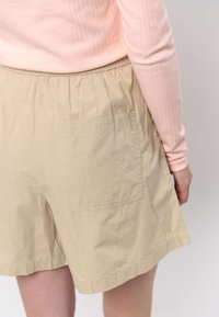 Bézs rövidnadrág rugalmas derékpánttal és hátul zsebbel. Az anyag könnyű súlyú, enyhén gyűrött textúrájú.