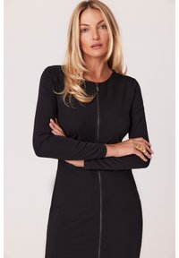 Czarna dopasowana sukienka z długimi rękawami, okrągłym dekoltem i zamkiem z przodu. Gładka tekstura i przylegający do ciała fason. Prosty i elegancki styl.