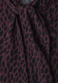 Tissu violet foncé avec des taches léopard noires irrégulières, rassemblé et drapé pour montrer la texture et les détails du motif.