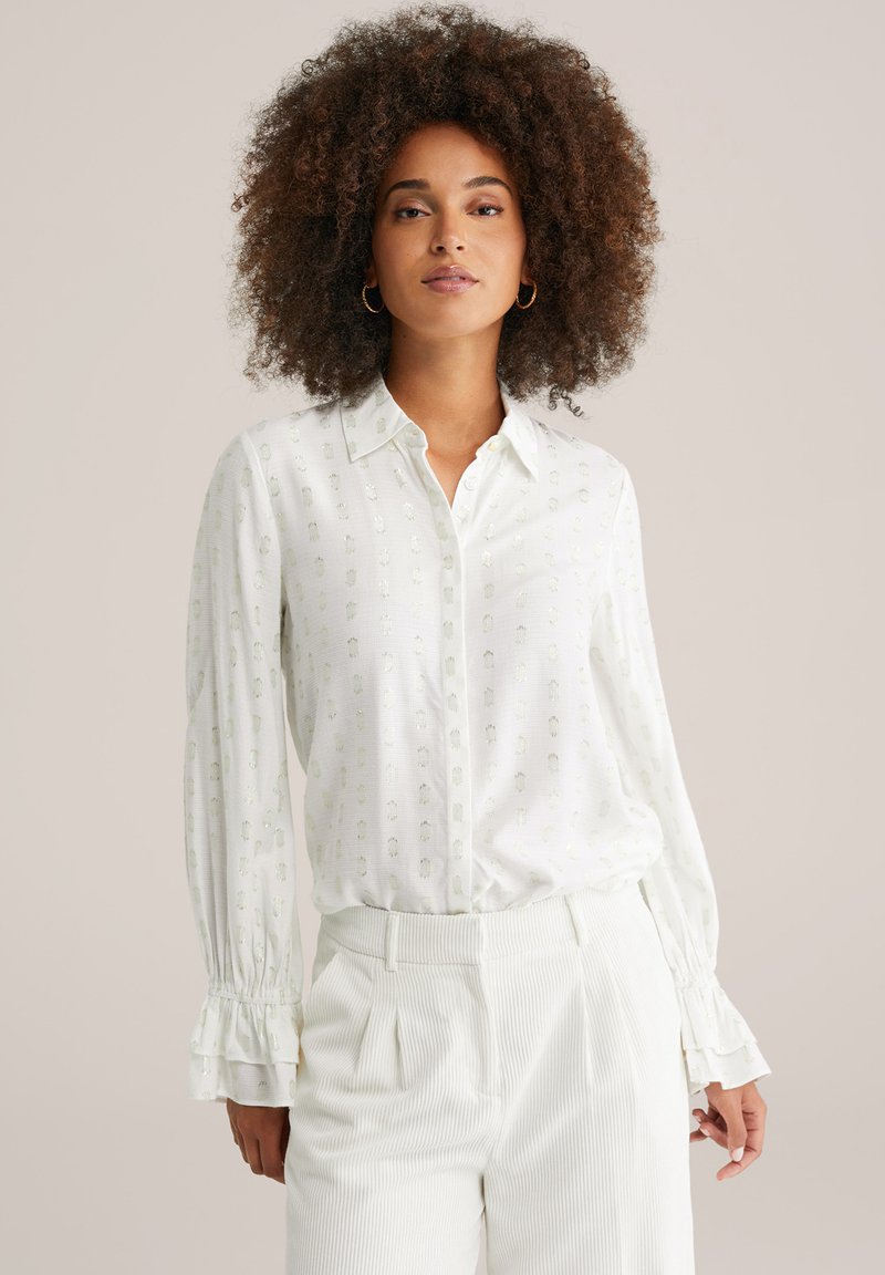 Camicia bianca con un delicato motivo a stampa e colletto a bottoni. Presenta maniche lunghe con polsini arricciati e una vestibilità comoda.