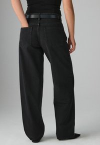 Svarta vida jeans i denim. Med två bakfickor och ett svart läderbälte. Enkelt mönster med en slät, matt yta.