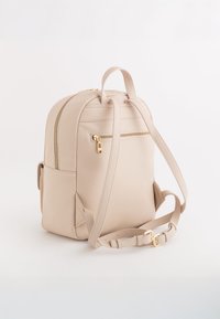 Mochila de cuero beige con un diseño redondeado, superficie texturizada, doble cremallera, bolsillo frontal y correas ajustables con acentos dorados.
